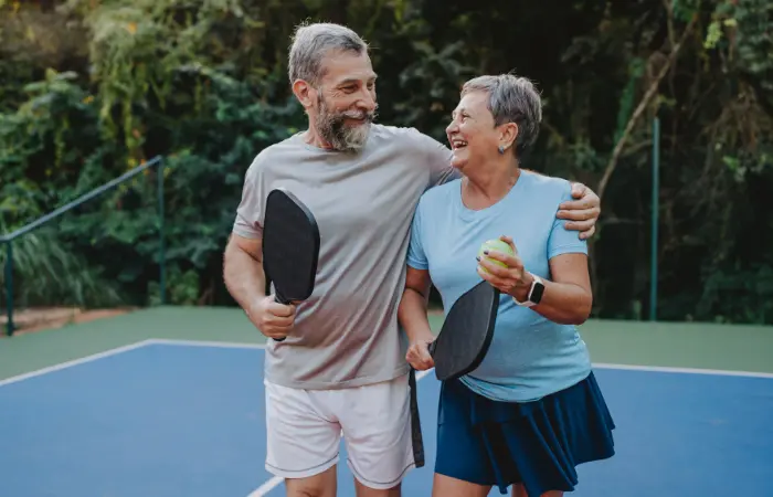 older couple hugging on tennis court and smiling for some reason